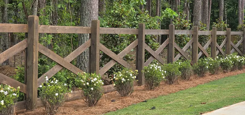 Stained wood crossbuck ranch fence lined with gardenias and pine straw