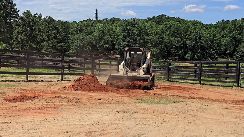 Skid steer pushing red clay to regrade a fenced pasture