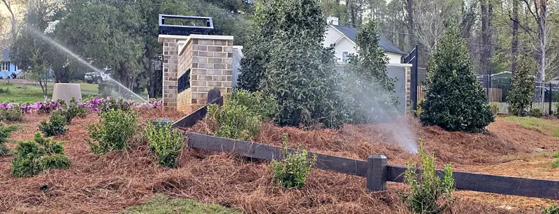Rotor and spray heads watering new shrubs and pine straw beds at a community entrance