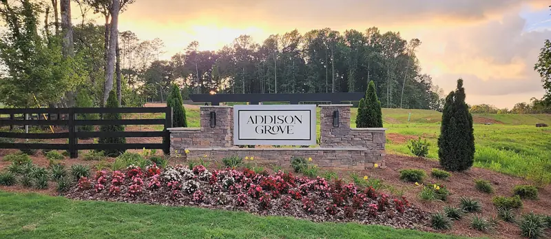 Stone entrance sign for a new community with seasonal flower beds, shrubs and fresh mulch at sunset