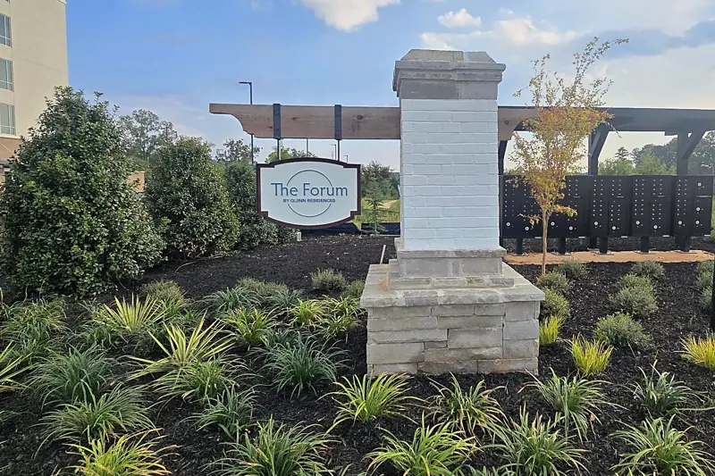 Community entrance with a stone column, mass plantings of liriope and shrubs, and fresh black mulch