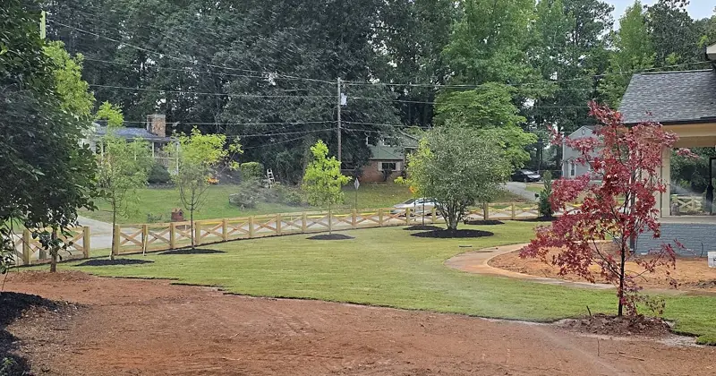 Newly laid sod lawn with new trees in mulch rings and a wood crossbuck fence